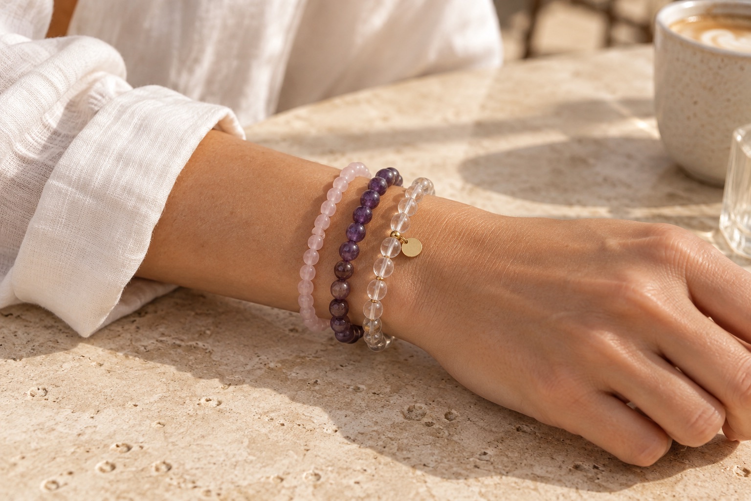 Pink, purple, and clear beaded bracelets stacked beside an ivory linen cuff.